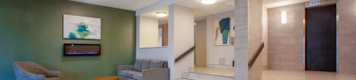 Lobby with lounge seating and staircase with elevators in the background at Northgate Tower Apartments in Woodstock, Ontario