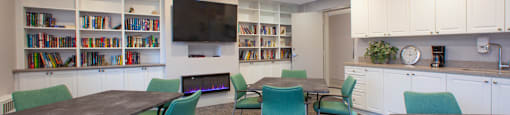 Social room with tables and chairs, flat screen TV with a fireplace below and library at Northgate Tower Apartments in Woodstock, Ontario