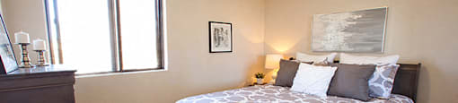 Mountain View Bedroom with window on the left. A big soft bed is in the middle of the room, with a painting hung above the headboard and a lamp on a nightstand beside it in Collingwood, ON