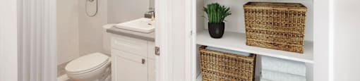 Linen closet with baskets and white towels with bathroom seen in the background at Riverbend Tower Apartments in Chatham, ON