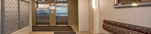 Lobby, looking towards elevators, with bench seating on right side and mailboxes on left side, at Riverbend Tower Apartments in Chatham, ON