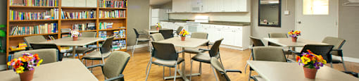 Lord Simcoe Apartments social room with tables and chairs, bookshelf filled with books, and
