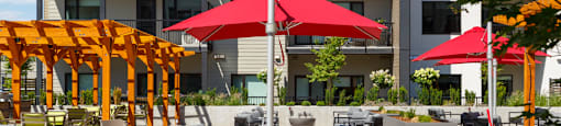 A patio with grey couches, red umbrellas, and a fire pit at The Ambrosi in Kelowna, BC.