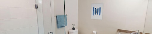 A white toilet sits in a bathroom next to a glass-enclosed walk-in shower in a renovated 3 bed 2 bath suite at Somerset Place in London, ON.