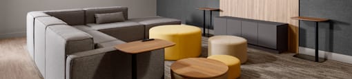 A modern social room with a grey sofa, yellow ottoman, and a wooden tv stand at The Ambrosi in Kelowna, BC.