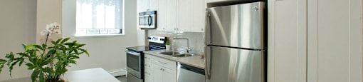 Sunnidale Place Finished kitchen with cupboards, washing machine, microwave, and stove. Apples sit in a bowl to the left in Barrie, ON