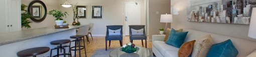 Sunnidale Place Living room with view of kitchen. Three stools are next to the counter and in the middle is a glass coffee table in Barrie, ON