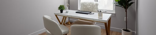 A white desk with a lamp and two chairs in a room at The Ambrosi in Kelowna, BC.