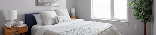 A bedroom with a bed, nightstand, and a plant at The Ambrosi in Kelowna, BC.