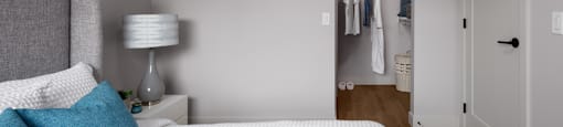 A bedroom with a bed, pillows, a lamp, and a closet at The Ambrosi in Kelowna, BC.