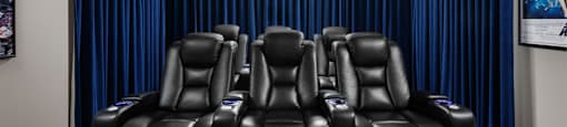 A theatre room with a row of black leather recliner chairs with blue curtains at The Ambrosi in Kelowna, BC.