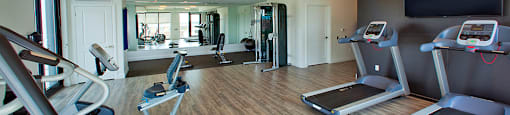 Fitness centre with cardio machines and free weight, yoga/stretching area seen in background at Trio on Belmont (Building B) in Kitchener, ON