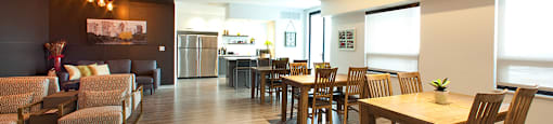 Penthouse resident's lounge with a large dining area with tables and chairs and a caterer's kitchen in the background at Trio on Belmont in Kitchener, ON