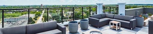 A rooftop patio with outdoor padded sectional couches and a view of the city at Trio on Belmont in Kitchener, ON