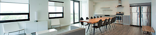 Social room with lounge area, large dining table and chairs and full kitchen located in Building C at Trio on Belmont in Kitchener, ON