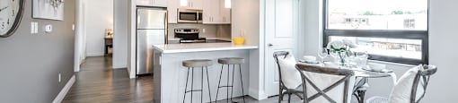 Dining area with table and chairs looking towards kitchen with bar stools at a breakfast bar Open-concept dining and living area looking towards patio door in a 2 bed + den 2 bath variation E in building A at Trio on Belmont in Kitchener, ON