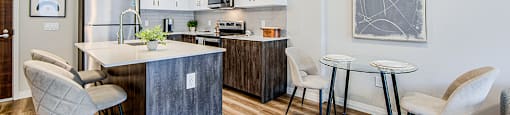 Dining area and kitchen with a two-seater dining table, kitchen island, wood-look lower, white upper and stainless steel appliances in a 2 bedroom 2 bathroom variation C layout at Vale Station Apartments in Waterloo, Ontario