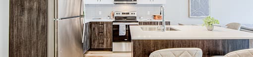 View of a kitchen with wood-look lower and white upper cabinets and a kitchen island with two bar stools in a 2 bedroom 2 bathroom variation C layout at Vale Station Apartments in Waterloo, Ontario