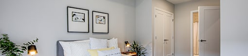 Primary bedroom with a large bed, bedside tables and two framed pictures on the wall in a 2 bedroom 2 bathroom variation C layout at Vale Station Apartments in Waterloo, Ontario