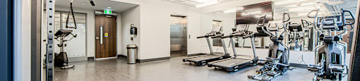 A spacious gym with a variety of equipment and an elevator that connects to a Yoga and Pilates studio on the floor above at Vale Station Apartments in Waterloo, Ontario.