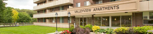 Exterior entrance of Valleyview Apartments with wooden benches and healthy flowerbeds