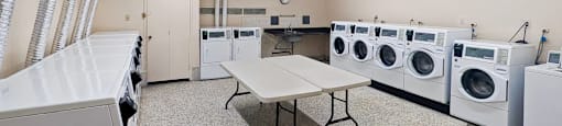 Laundry room with multiple full-sized washer and dryers with folding table at Village Tower Toronto ON