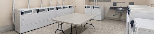 Laundry room with multiple full-sized washer and dryers with folding table at Village Tower Toronto ON