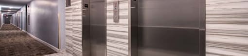 Two stainless steel elevators in a hallway with marble flooring.