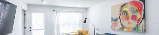 A living room with a blue couch, a yellow chair, and a painting on the wall.
