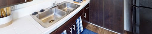 a kitchen with a stainless steel sink and wooden cabinets at The Marquee Apartments, North Hollywood, California