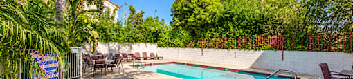 A pool surrounded by chairs and trees.