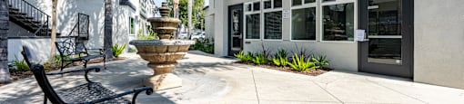 A black bench is in front of a building with a fountain in front of it at The Marquee Apartments, North Hollywood, CA 91605