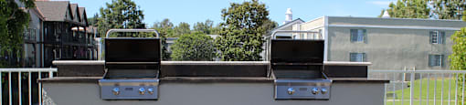 A white outdoor grill with two burners is in the middle of a gravel area.