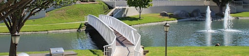 A park with a bridge over a pond and a fountain.