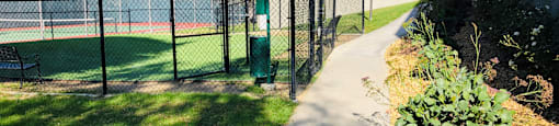 A walkway leads to a building with a tennis court behind a fence.