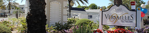 A Versailles sign is in front of a building and some trees.