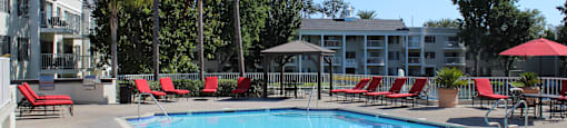 A swimming pool surrounded by red chairs and trees.