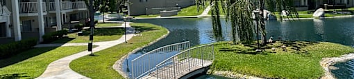 A small pond in a grassy area with a bridge leading to it.