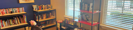 A room with a carpeted floor, a chair, and a bookshelf filled with books.