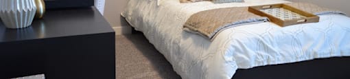 A bed with a white comforter and a tray with a book on it.