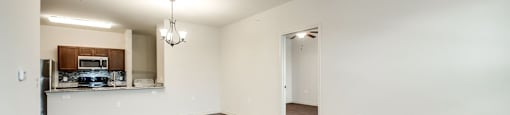 A room with a ceiling fan and a kitchen area in the background.