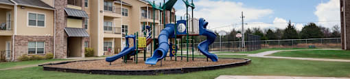 Playground with a blue slide and a green slide in front of apartment buildings.