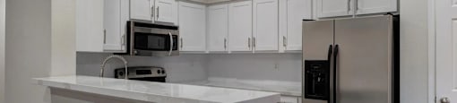 A kitchen with white cabinets and a stainless steel refrigerator.