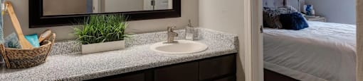 A bathroom with a sink, mirror, and a bedroom in the background.