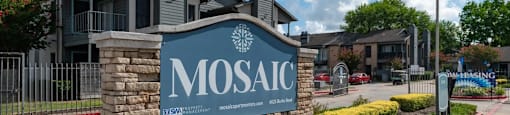 The image shows a sign for MOSAIC in front of a building with a flag on a pole.