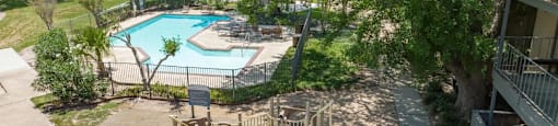 A playground with a slide and swings is surrounded by a fence and a pool.