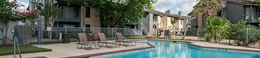 A swimming pool surrounded by trees and chairs.