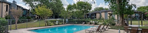 A swimming pool surrounded by trees and chairs.