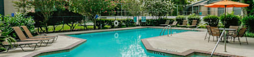 A swimming pool surrounded by trees and chairs.