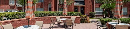A patio with tables and chairs and umbrellas in front of a red brick building.